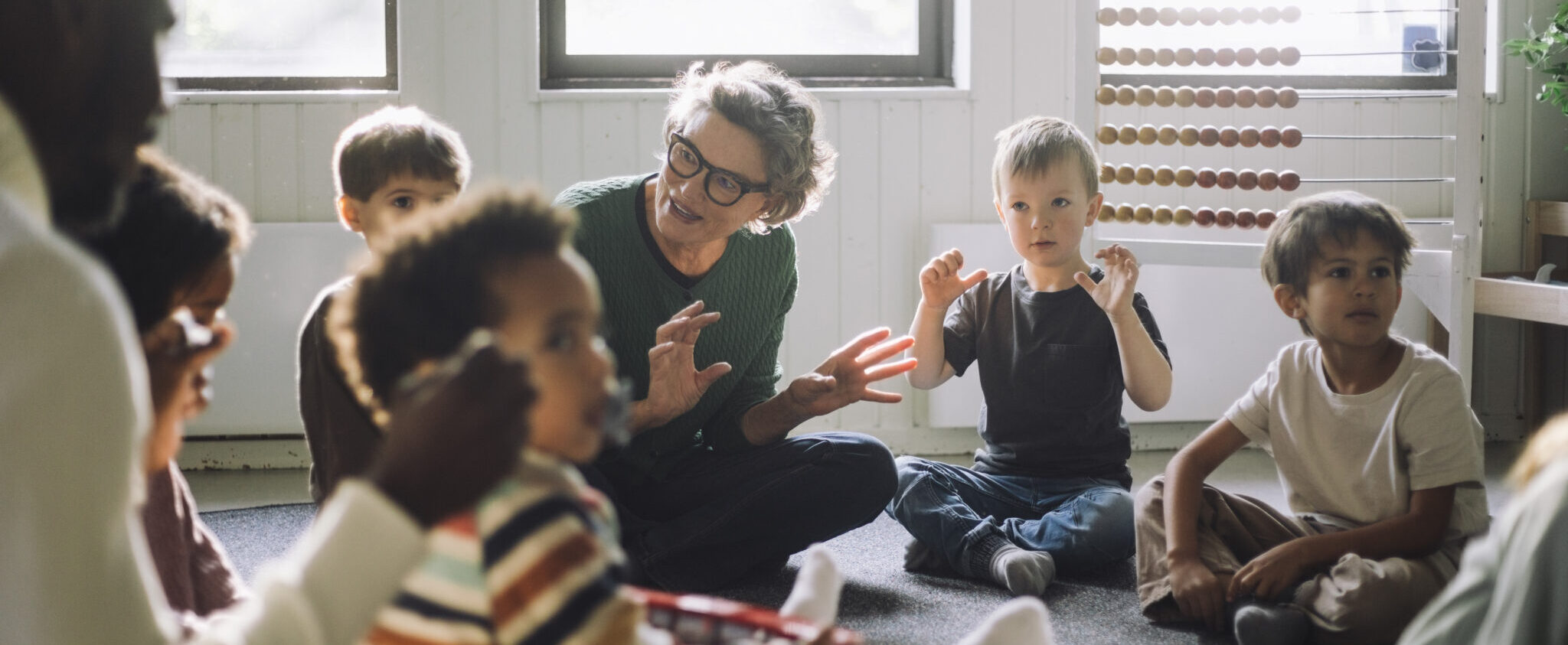 Senior female teacher playing with group of preschool children while sitting in classroom at kindergarten Outpatient Clinic for Children, Adolescents and Adults